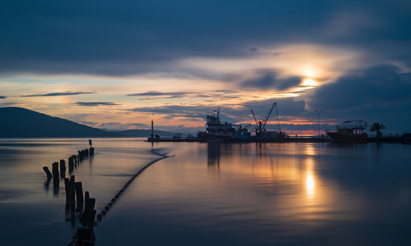 Pier poles extending into the sea. Sunset, clouds and fishing boats on the horizon. Photographed with long exposure.