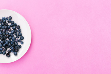 Juicy blueberries. White plate with summer berries on a pink background. Healthy breakfast food or cooking ingredients.