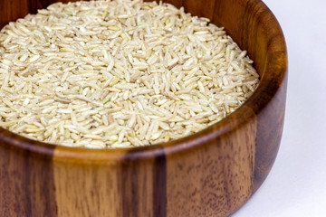 Uncooked brown rice in a wooden bowl on white background