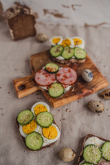 Set of sandwiches with rye bread, egg, ham, cucumber, cream cheese, seeds and spices on a wooden board. Rustic breakfast.