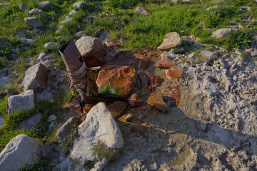 iron pipe flowing clean drinking water . spring water from the ground Colorfull red stone . Water flowing from pipe against blurred mountain background.