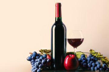 Glass and bottle of red wine with grapes and apples. Red wine on a light background