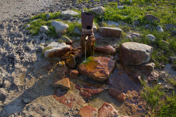 iron pipe flowing clean drinking water . spring water from the ground Colorfull red stone . Water flowing from pipe against blurred mountain background.