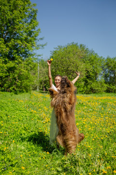 A red hair girl and her pet briard are playing and doing exercises on the green grass in spring.