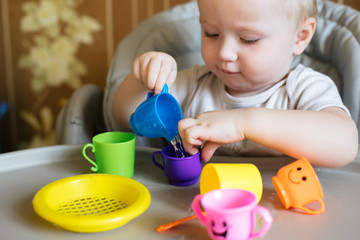baby pours water from cup into jug. girl plays with toy utensil. child plays with improvised materials. Early development concept