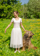 A red hair girl and her pet briard are playing and doing exercises on the green grass in spring.