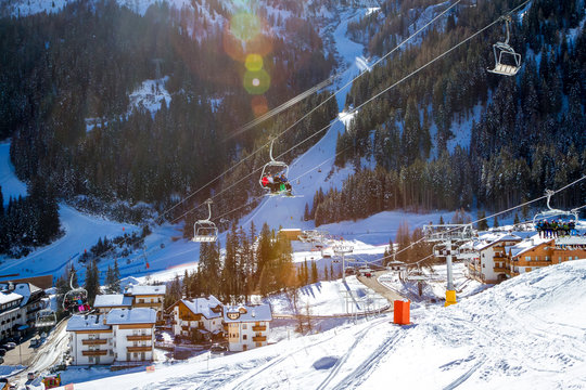 View of Arabba village and chair lift with skiers on a sunny winter day. Sellaronda, Dolomiti Superski.