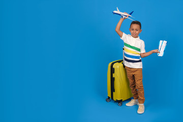 African-American traveler boy is ready for the trip, showing passport and plane tickets is happy, yellow travel bag, has a special offer from a travel company, on a blue background.