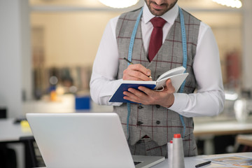 Male tailor standing near laptop, making notes