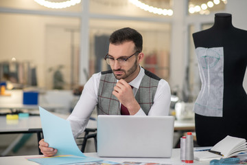 Naklejka premium Male tailor sitting at laptop, propping chin on hand