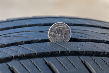 Closeup of checking tire tread wear depth of old tire using a quarter coin. Concept of automobile...