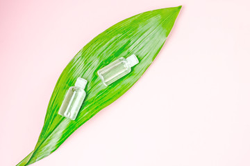 Green cosmetics, body care products.Two transparent cosmetic bottles on a large green leaf of a plant on a pink background, top view, copy space.The concept of organic cosmetics and natural skin care