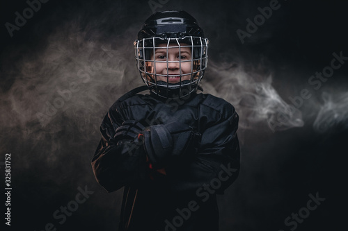 Young Blonde Fit Boy Ice Hockey Player Posing In A Dark Studio For A Photoshoot Wearing An Ice Skating Uniform With Helmet Holding Hands Crossed While Smiling On Camera Close Up Portrait Young Blonde Fit Boy Ice Hockey Player Posing In A Dark Studio For A Photoshoot Wearing An Ice Skating Uniform With Helmet Holding Hands Crossed While Smiling On Camera Close Up Portrait