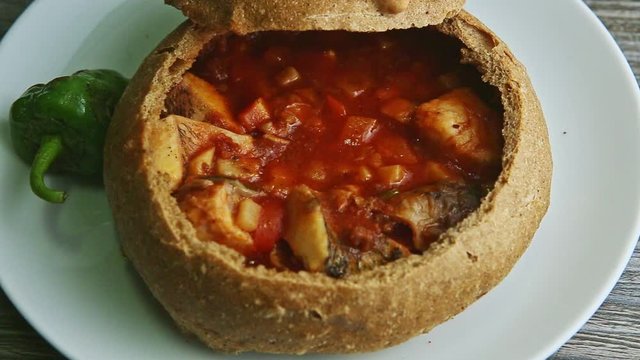 closeup focus out from finely decorated fish soup in brown bread bowl on white plate
