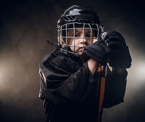 Young blonde sporty boy, ice hockey player, posing in a dark studio for a photoshoot, wearing an...