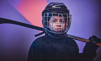 Young blonde sporty boy, ice hockey player, posing in a bright neon studio for a photoshoot,...