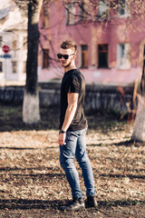 Handsome young man with a beard and stylish haircut in sunglasses in fashionable clothes. Street Lifestyle.