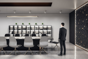 Businessman standing in conference interior hall with books on shelf.
