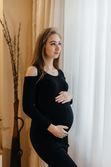 A beautiful pregnant girl is standing in a room near the window