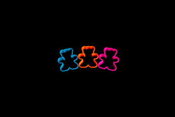 Three multi-colored plastic cookie cutter for making cookies in the form of a teddy bear on a black...