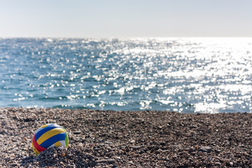 Obraz premium Colored children's ball on a sea pebble beach on background of a sea a sunny day.