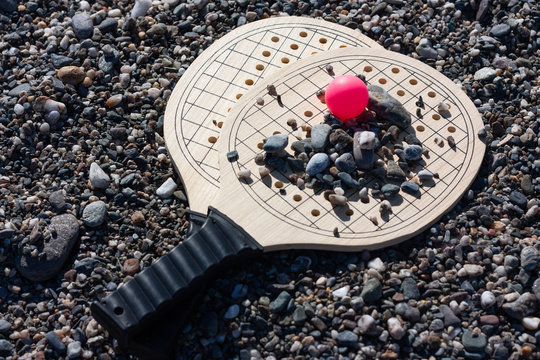 Set for game of beach tennis, wooden rackets with a pink ball on background di pabble beach.