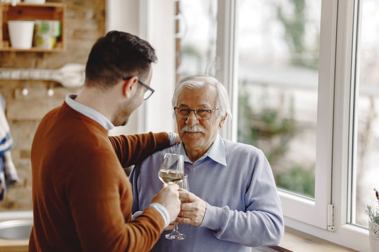 Happy senior man drinking wine with his adult son.