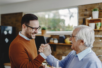 Happy man and his senior father giving each other manly greet in the kitchen.