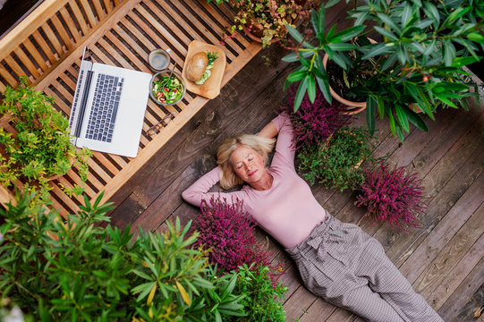 Top view of senior woman with laptop lying outdoors on terrace, resting.