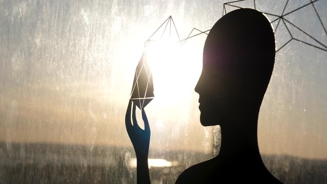 Female black silhouette against glass window with a strange object in her hand. Stock footage. Sun shining through the female shape, the third eye and soul enlightenment concept.