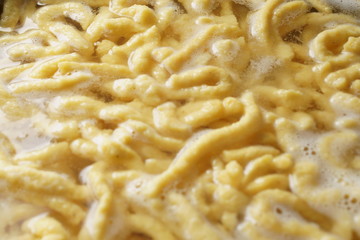 a pile of homemade swabian spaetzle pasta noodles cook in a pot in hot water