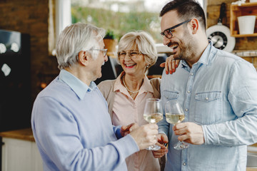 Happy senior parents and their adult son drinking wine and having fun in the kitchen.