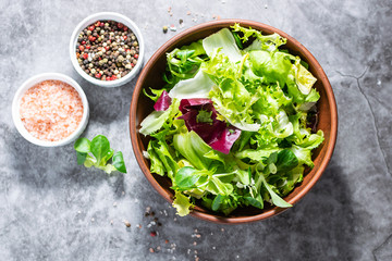 Fresh green salad mix with olive oil and Himalaya salt on dark stone table top view. Healthy food concept.