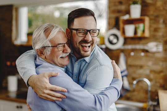 Cheerful man and his senior father embracing while greeting in the kitchen.