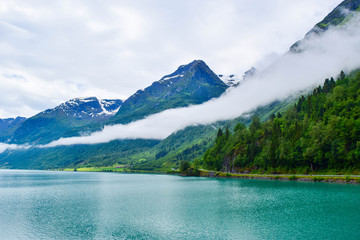 Obraz premium Landscape of beautiful Oldevatnet glacial lake and foggy mountains in which there are glaciers of Jostedalsbreen National Park. Norway.