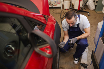 High angle view at car mechanic checking pressure in tires during vehicle inspection in garage shop, copy space