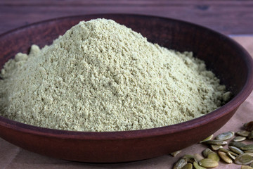 Pumpkin seed flour in a clay plate on a dark wooden background.