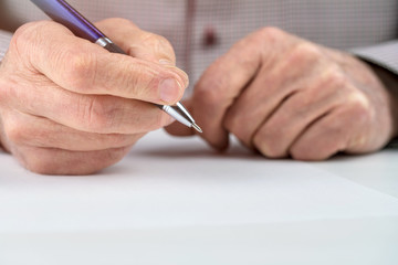 pensioner holds pen above blank paper on white table