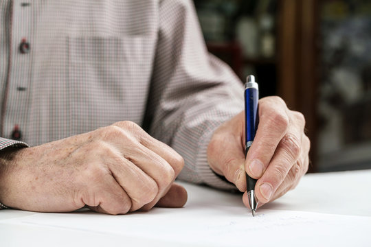 left handed senior man writes letter on paper sheet at table