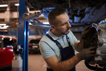 Waist up portrait of bearded car mechanic repairing gearbox in auto workshop, copy space