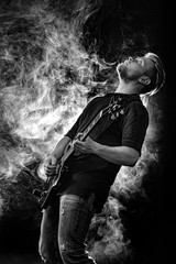 Handsome young musician man playing on guitar and singing in the smoke on stage or scene.