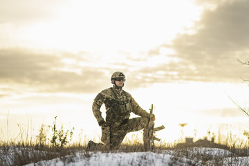 Modern soldier in the winter desert put gun on the ground and knelt down. full equipment commandos with helmet and weapon. atmosphere after moder special force battle