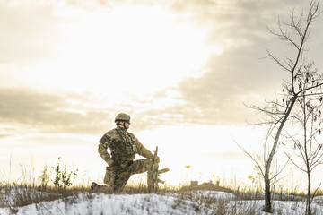 Modern soldier in the winter desert put gun on the ground and knelt down. full equipment commandos with helmet and weapon. atmosphere after moder special force battle