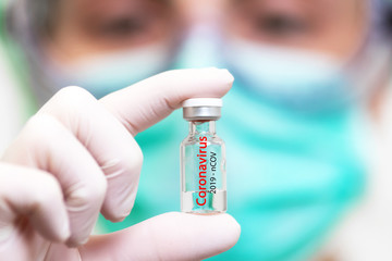 A doctor in medical gloves and mask holding an ampula with vaccine. Close up shot. Coronavirus, epidemic and medicine concept .