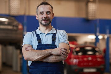 Waist up portrait of mature car mechanic standing with arms crossed while posing in auto repair...