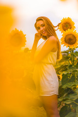 Blonde among beautiful sunflowers with a white dress