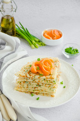 Traditional Russian thin pancakes or crepes with cheese, herbs and smoked salmon on a white plate on a light background. Holiday maslenitsa. Vertical orientation.