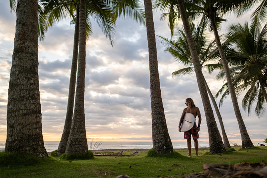 Man standing with surfboard on beach during sunrise