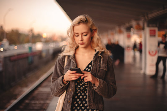 Young woman using smart phone waiting for train at subway station