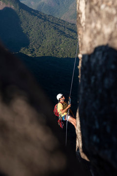 Man rappelling steep rocky mountain with beautiful view to rainforest